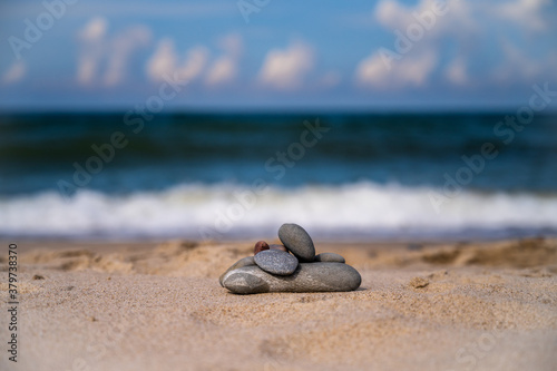 A pyramid made of stones on yellow sand on the seashore, against the background of white waves of the surf