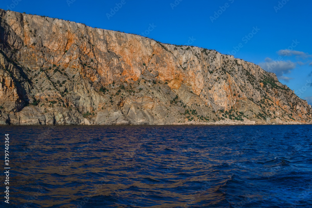 red orange stone rock stands on shore of the blue sea on bright sunny day, summer sky with clouds