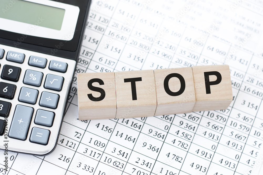 STOP word concept written on wooden cubes blocks lying on a light table next to calculator and pen STOP word concept written on wooden cubes blocks lying on a light table next to calculator and pen