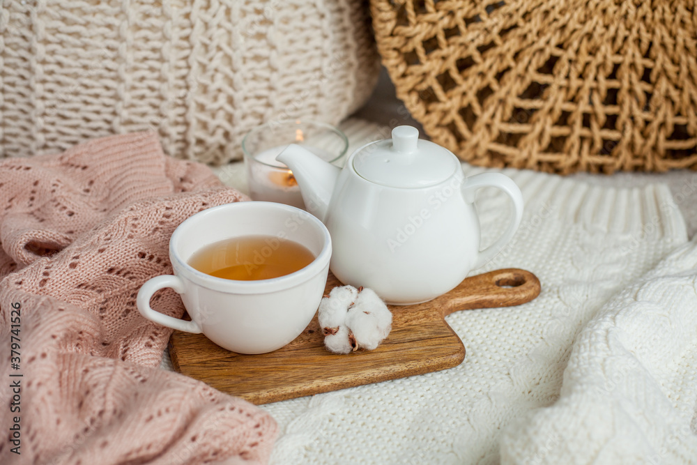 A mug of hot tea, a teapot, a wooden stand on an ottoman. Cozy autumn. Winter breakfast. Cotton. A mug of hot tea, a teapot, a wooden stand on an ottoman. Cozy autumn. Winter breakfast. Cotton.