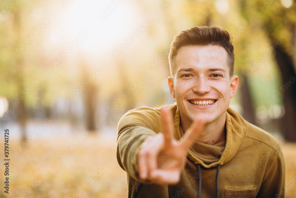 Obraz premium Portrait of a handsome guy smiling and showing peace in the autumn park