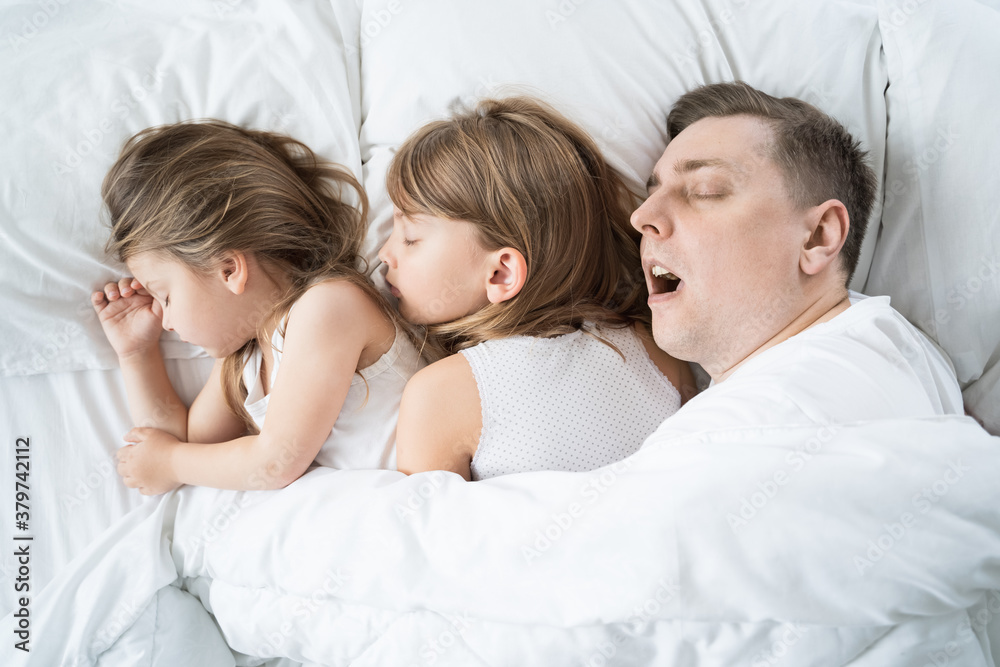 Kids, daughters, dad sleep together in bed on pillows under blanket. Father is snoring hard. Family joint sleeping. Insomnia, night bedtime.Sweet dreams. arly wake up,rise to kindergarten,school,work Kids, daughters, dad sleep together in bed on pillows under blanket. Father is snoring hard. Family joint sleeping. Insomnia, night bedtime.Sweet dreams. arly wake up,rise to kindergarten,school,work