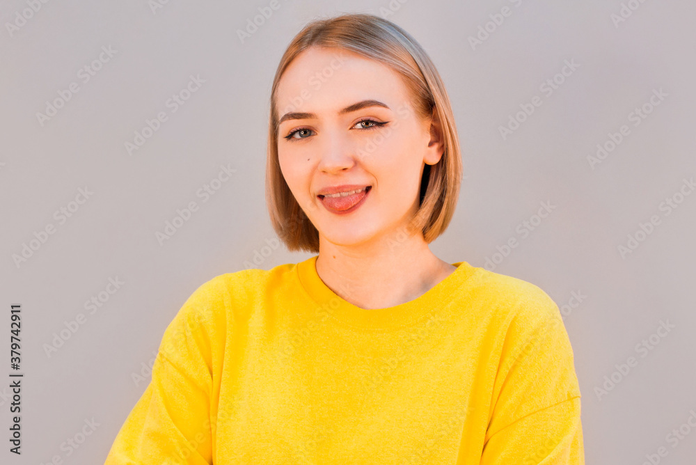 Funny cute young girl smiling winking showing tongue looking at camera over gray background. Funny cute young girl smiling winking showing tongue looking at camera over gray background.