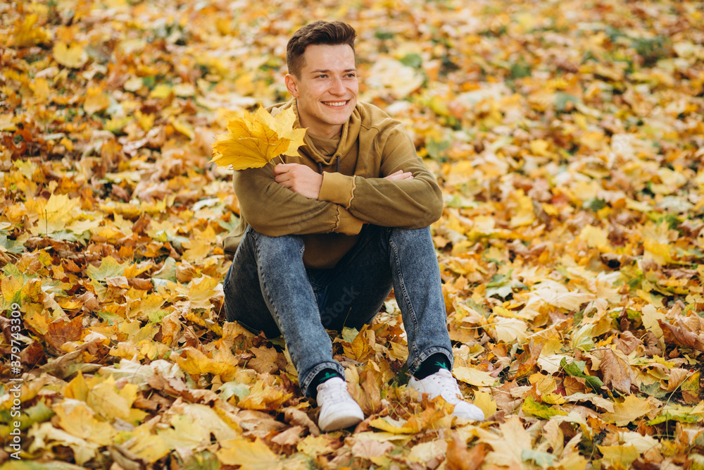 Portrait of handsome and happy boy with a bouquet of yellow leaves smiling and dreaming in the autumn park