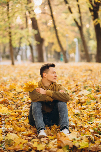 Portrait of handsome and happy boy with a bouquet of yellow leaves smiling and dreaming in the autumn park