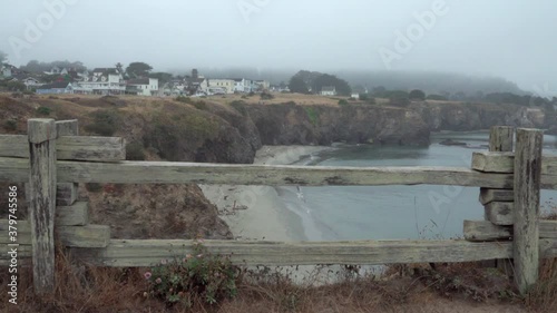 A wooden fence frames a foggy morning view of small beach and the historic wooden buildings of Mendicino, California. photo