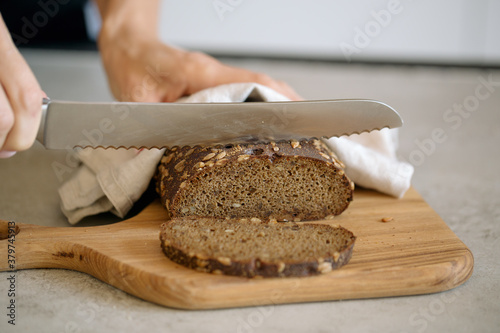 The process of slicing bread with seeds on a wooden cutting Board, linen napkin, hand movement, knife in hand.