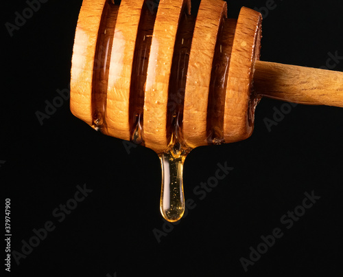 Honey dripping from wooden honey dipper on black background.