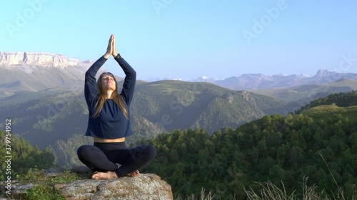 Young woman practices yoga high in the mountains. Sunset. 