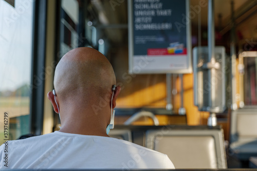 Fotografi Interior and selected focus view at the back of male passenger with face protection mask and skinhead who sit in  tram or train in Germany during epidemic of COVID-19 virus with new normal concept