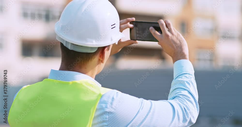 Worker at construction site making photos on his cell phone, back view, tracking shot