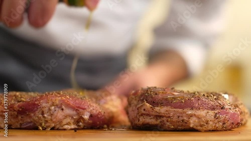 Chef prepares a delicious lunch or dinner in the kitchen at home. Cooking grilled meat. The cook pours oil on two raw spiced steaks on a wooden Board. Preparing for a barbecue picnic