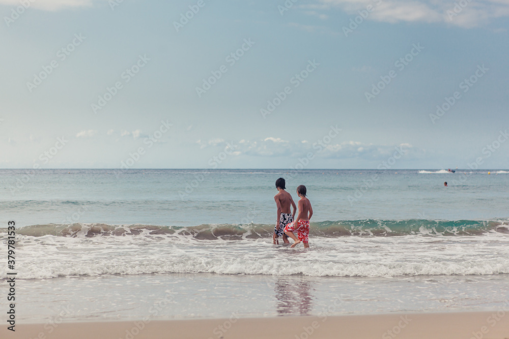 Two boys in swimming shorts walking into the ocean in the summer Two boys in swimming shorts walking into the ocean in the summer