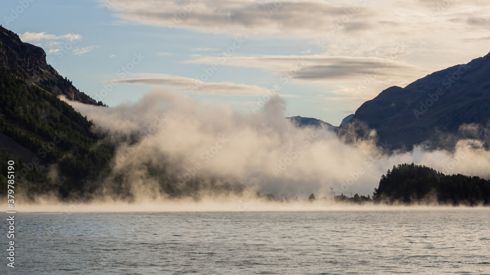 Maloja mountain Pass, Switzerland. Landscape of the lake Sils in the morning during the fall time. The fog covers the lake and the shores. Traditional Swiss contest. Natural landscape