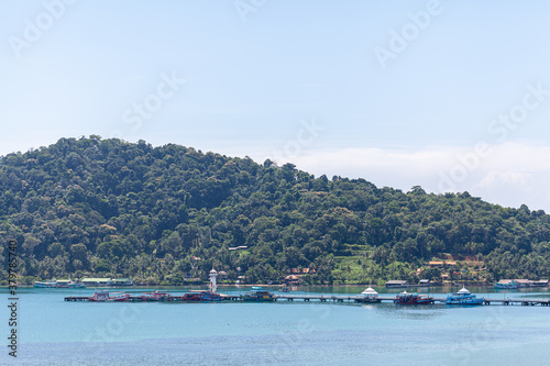 Fototapeta Naklejka Na Ścianę i Meble -  Beautiful summer landscape of the resort with turquoise sea water, village , hotels and mountains on the horizon, yellow flowers and blue sky. Thailand
