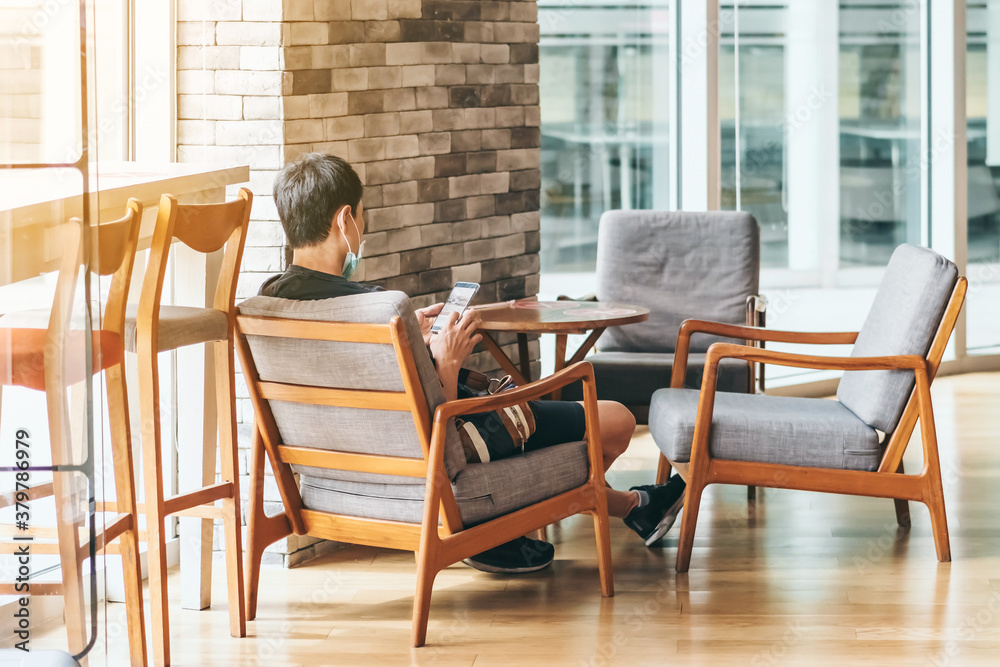 Back view of Asian man use smartphone and relax in coffee shop, where seats are spaced for social distancing during the Corona virus (COVID-19) epidemic. New normal lifestyle Back view of Asian man use smartphone and relax in coffee shop, where seats are spaced for social distancing during the Corona virus (COVID-19) epidemic. New normal lifestyle