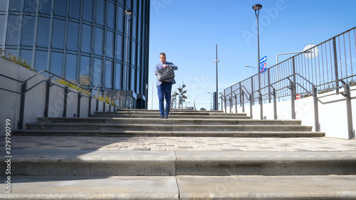 Celebrating success. Low angle view of excited young businessman keeping arms raised and expressing positivity while standing outdoors with office building in the background