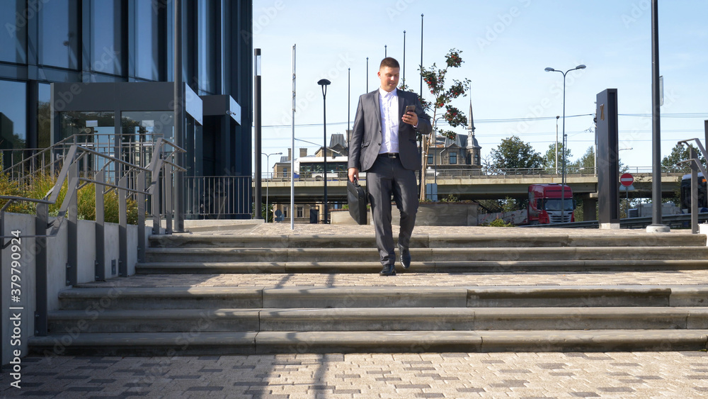 Celebrating success. Low angle view of excited young businessman keeping arms raised and expressing positivity while standing outdoors with office building in the background Celebrating success. Low angle view of excited young businessman keeping arms raised and expressing positivity while standing outdoors with office building in the background