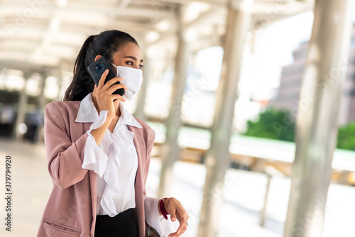 Business woman wear face mask talking via smartphone walking in the city smiling
