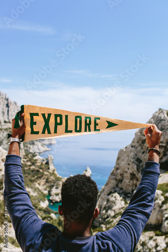 A man holding up an pennant that says Explore infront of cliff and ocean.