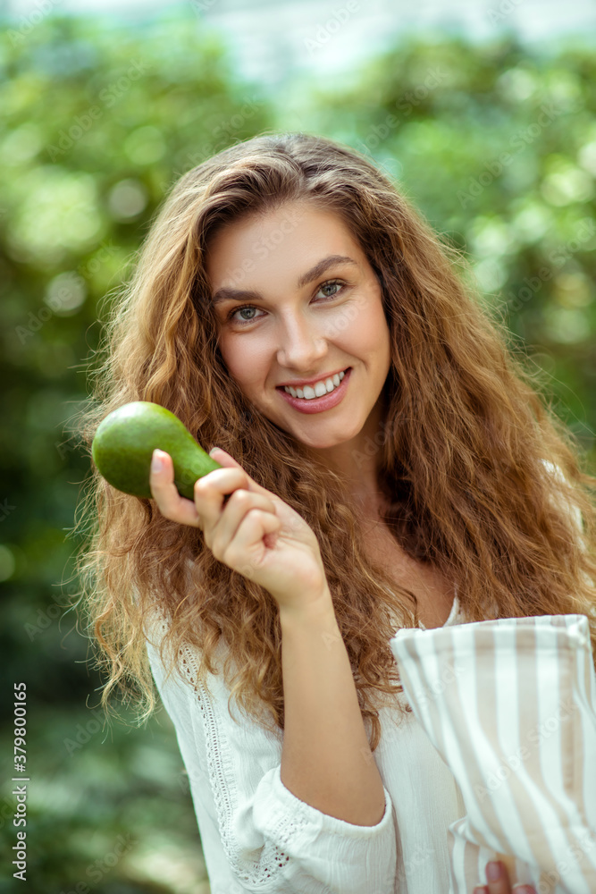 Woman in white shirt holding avocado and smiling Woman in white shirt holding avocado and smiling