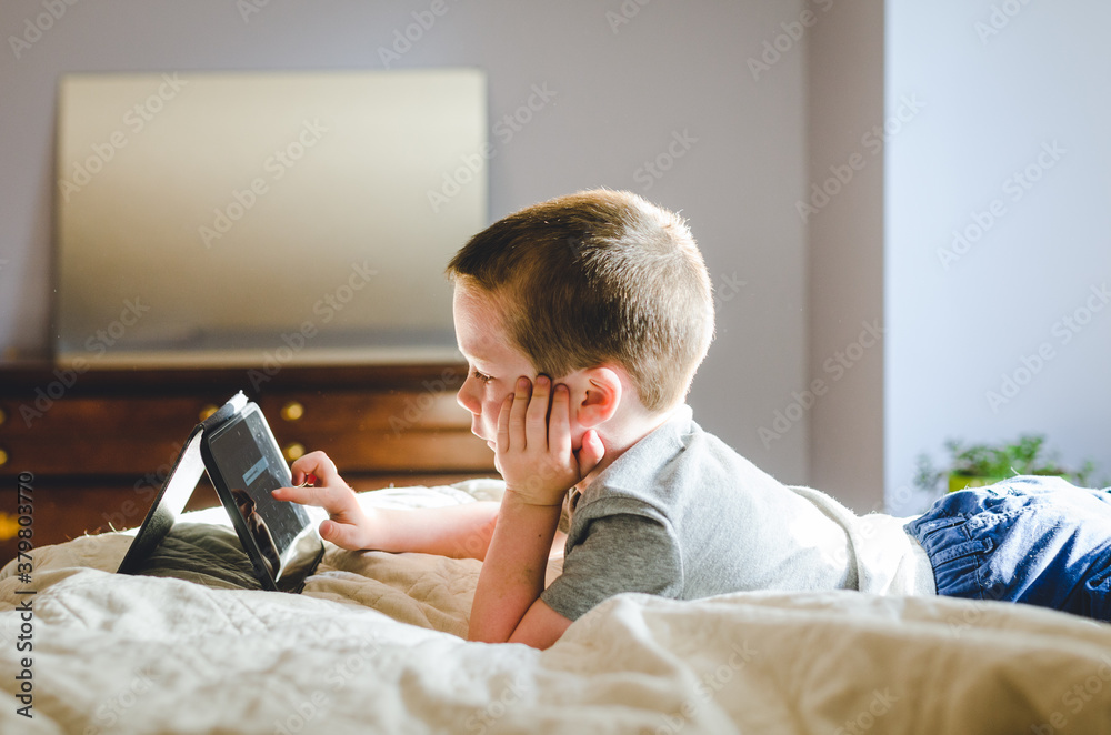 Young boy lying on bed playing with a tablet Young boy lying on bed playing with a tablet