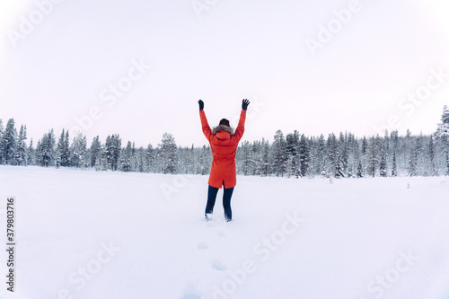 young girl in a bright warm orange jacket jumps from happiness up from a deep snow against a background of a beautiful winter forest