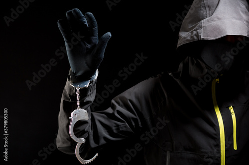 Closeup view of the hands of a burglar or hucker in black gloves with handcuffs on a black background photo