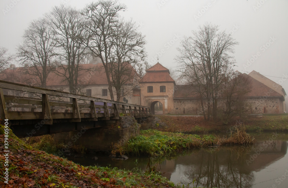 The restored old Shlokenbek manor in Latvia. View from the river bank on an autumn foggy morning The restored old Shlokenbek manor in Latvia. View from the river bank on an autumn foggy morning