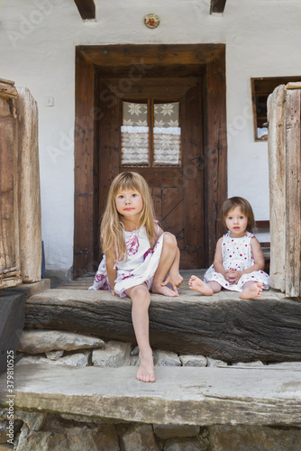 Little girls sitting down on stairs in front of traditional home photo