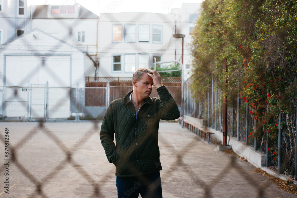 Middle aged male in fall attire photo through fence on playground while he pushes hair back Middle aged male in fall attire photo through fence on playground while he pushes hair back