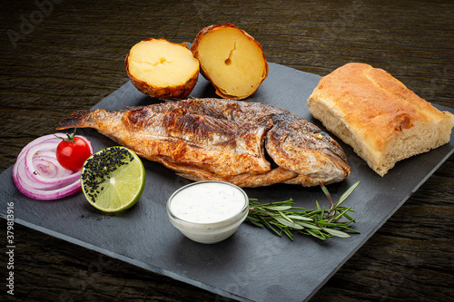 Grilled dorado with baked potatoes, matnakash and red sauce. Served on a stone plate photo