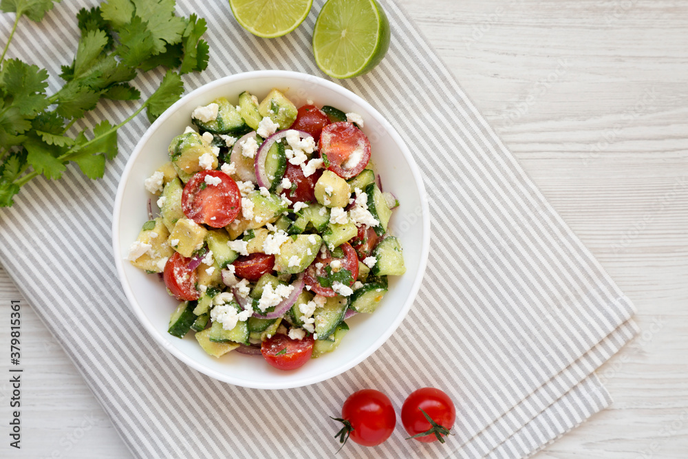 Delicious Avocado Tomato and Cucumber Salad in a bowl on a white wooden background, top view. Flat lay, overhead, from above. Copy space. Delicious Avocado Tomato and Cucumber Salad in a bowl on a white wooden background, top view. Flat lay, overhead, from above. Copy space.