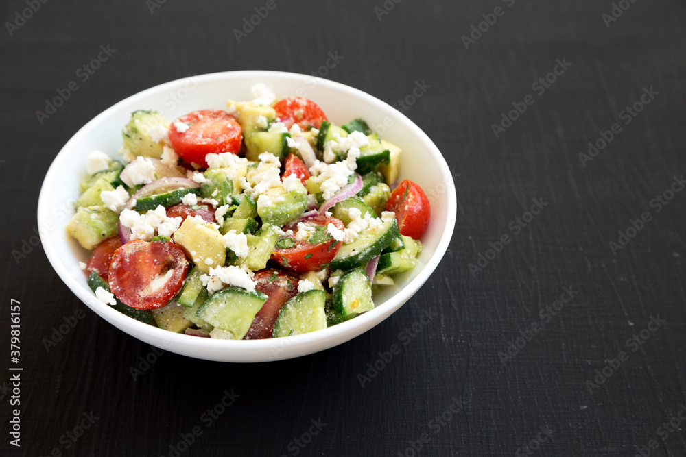 Delicious Avocado Tomato and Cucumber Salad in a white bowl on a black background, side view. Space for text. Delicious Avocado Tomato and Cucumber Salad in a white bowl on a black background, side view. Space for text.