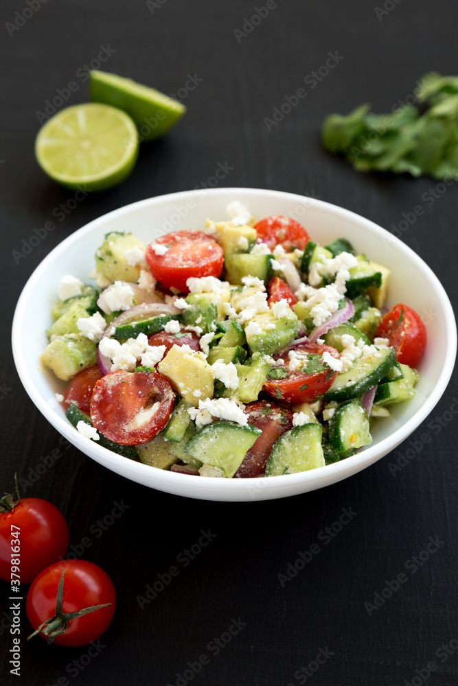 Delicious Avocado Tomato and Cucumber Salad in a white bowl on a black background, low angle view. Close-up.