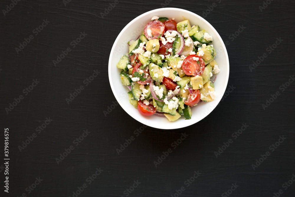 Delicious Avocado Tomato and Cucumber Salad in a white bowl on a black surface, top view. Flat lay, overhead. Copy space. Delicious Avocado Tomato and Cucumber Salad in a white bowl on a black surface, top view. Flat lay, overhead. Copy space.