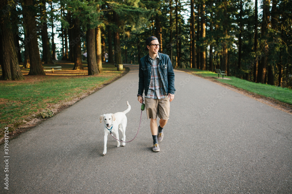 Man in his 20's taking his dog for a walk in the park