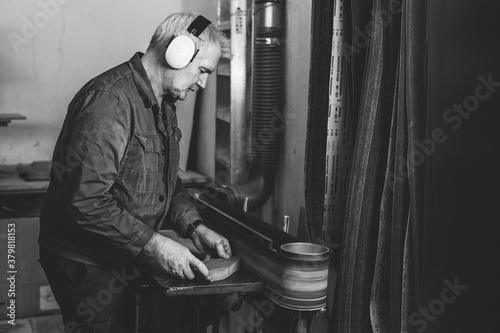 senior woodworker grinding a piece of wood on a belt sander in black and white