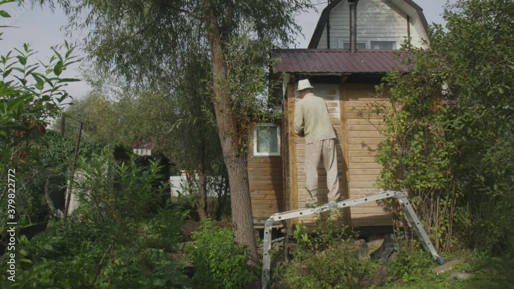 An adult man standing on the stairs repairs house in the open air, paints the exterior walls with white paint: lifestyle, home renovation and renovation concept. Painting. Rear view, slow motion, 4K An adult man standing on the stairs repairs house in the open air, paints the exterior walls with white paint: lifestyle, home renovation and renovation concept. Painting. Rear view, slow motion, 4K