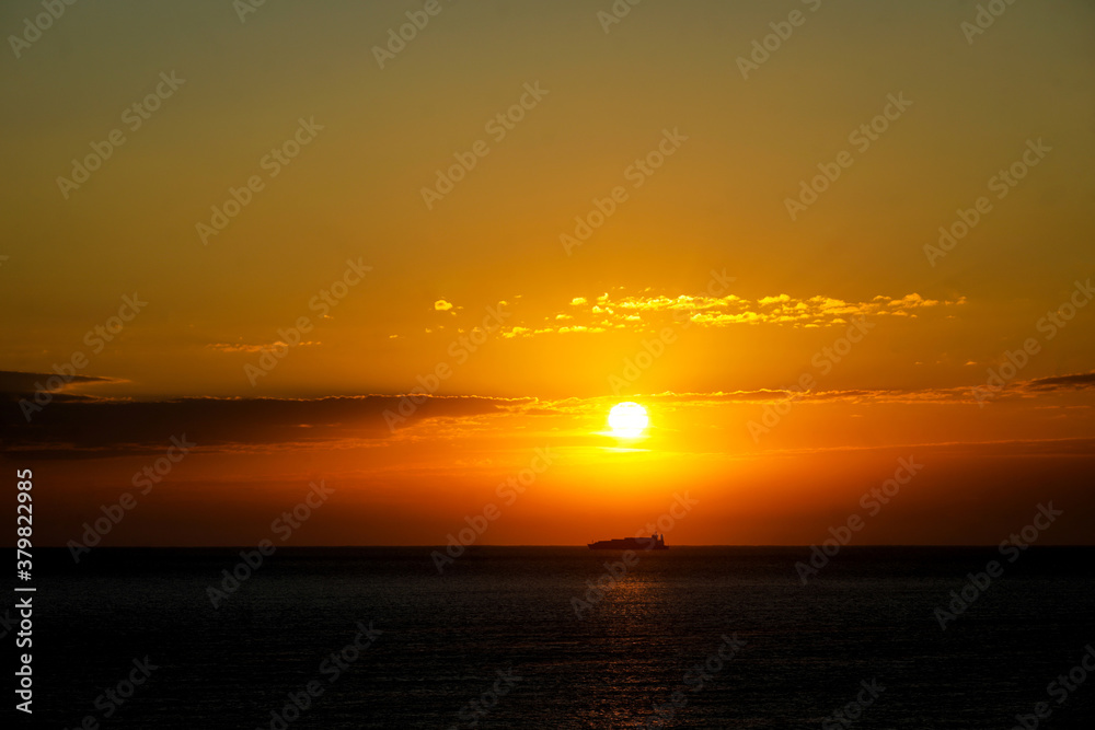 Sun rises over the Black Sea while a big cargo boat is passing by.