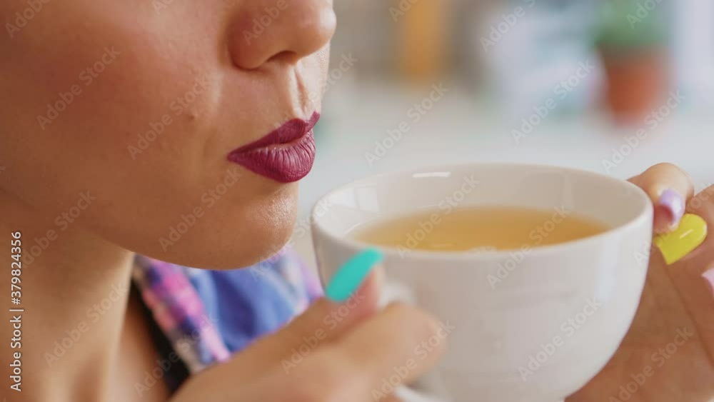 Cheerful woman drinking hot green tea in the morning. Close up of pretty lady sitting in the kitchen in the morning during breakfast time relaxing with tasty natural herbal tea from white teacup. Cheerful woman drinking hot green tea in the morning. Close up of pretty lady sitting in the kitchen in the morning during breakfast time relaxing with tasty natural herbal tea from white teacup.