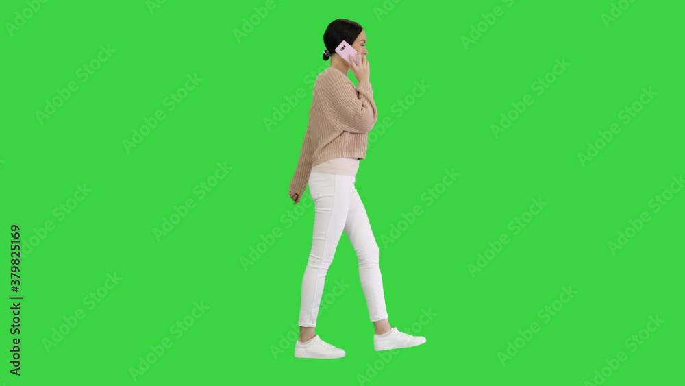 Smiling young woman talking on the phone while walking on a Green Screen, Chroma Key. Smiling young woman talking on the phone while walking on a Green Screen, Chroma Key.