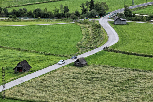 Curved road between two pastures with pair of cars