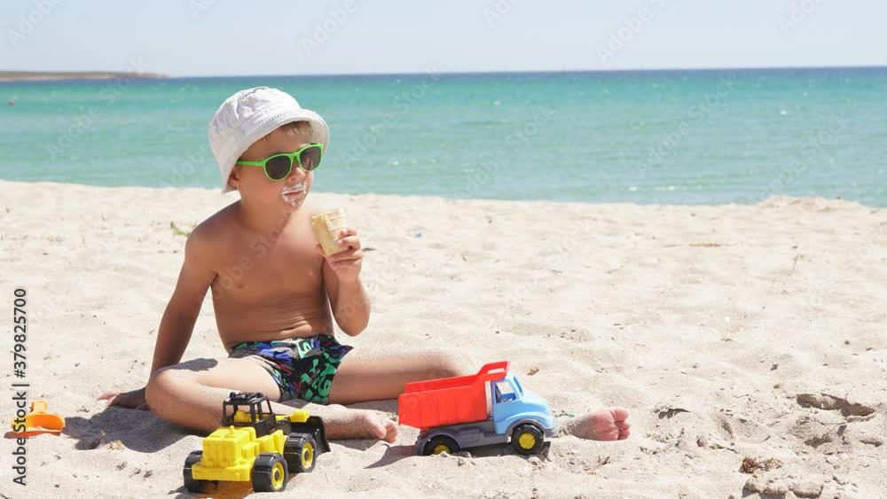 Happy baby eats ice cream on the beach and plays with the sand on the background of the azure sea. Happy baby eats ice cream on the beach and plays with the sand on the background of the azure sea.