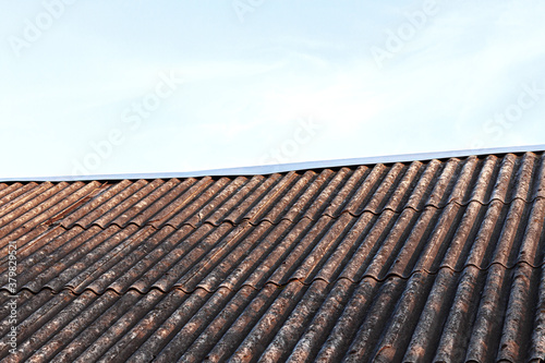 Old dirty gray slate roof against blue sky