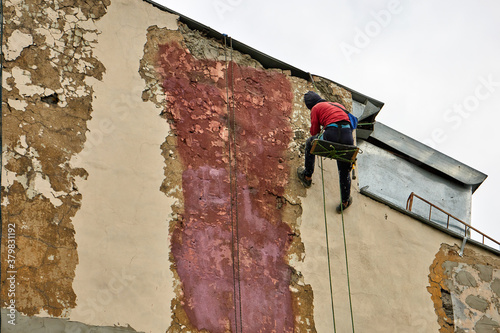 Working steeplejack with special equipment repairs the facade of the building. House walls cleaning and restoration works