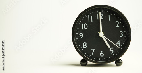 Decorative close-up black analog alarm clock for 5 o'clock or 17 o'clock, separate white background with copy space.