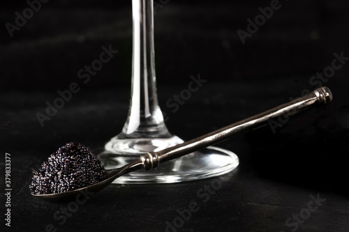Black caviar on a spoon with a glass of champagne, on a dark background with a place for text