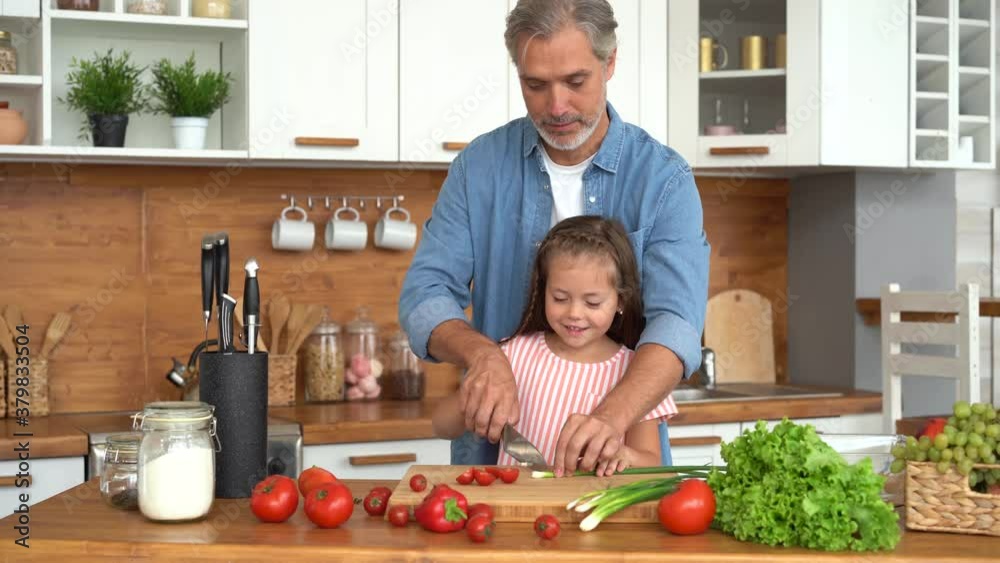 Father teaching cute kid daughter cutting fresh vegetable salad in kitchen. Single adult parent dad explaining child girl learning cooking healthy food prepare vegan meal together at home. Father teaching cute kid daughter cutting fresh vegetable salad in kitchen. Single adult parent dad explaining child girl learning cooking healthy food prepare vegan meal together at home.