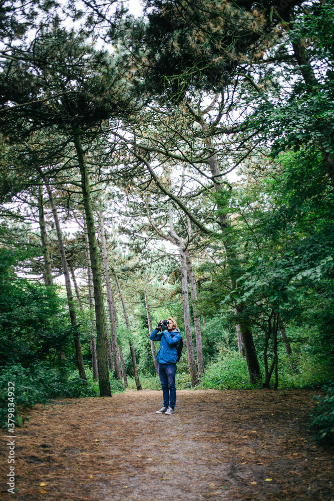 Young man taking a photo of the trees while standing on a path Young man taking a photo of the trees while standing on a path